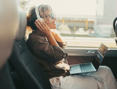 One woman listening music with headphones and computer sitting inside public bus transport enjoying travel transportation trip. Modern traveler. Happy free female people enjoying laptop device for job